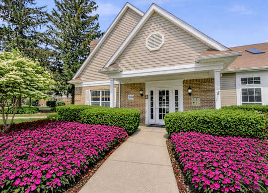 A house with a grey roof and a white door is surrounded by a flower bed.