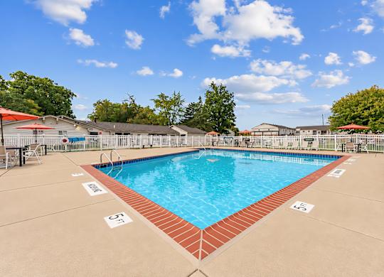 A large outdoor swimming pool with a red brick border and a clear blue sky above.