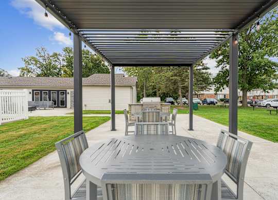 A grey table and chairs are set up under a metal roof.