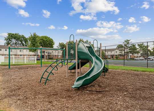 A playground with a green slide and a brown dirt ground.