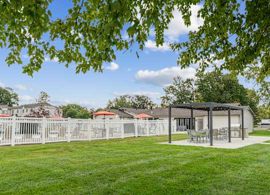 A white fence surrounds a green lawn with a pavilion in the background.