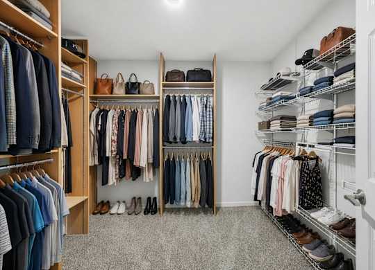 A walk-in closet with clothes and shoes organized on shelves and hangers.