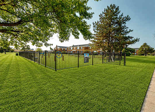 A black fence surrounds a green lawn with a building in the background.