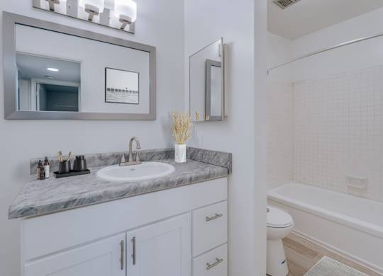 A bathroom with a marble countertop and white fixtures.