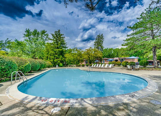 A round swimming pool surrounded by trees and chairs.