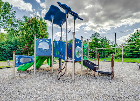 A playground with a blue slide, a green slide, and a wooden swing set.