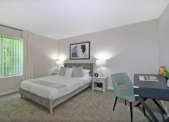 A bedroom with a bed, desk, chair, and window.