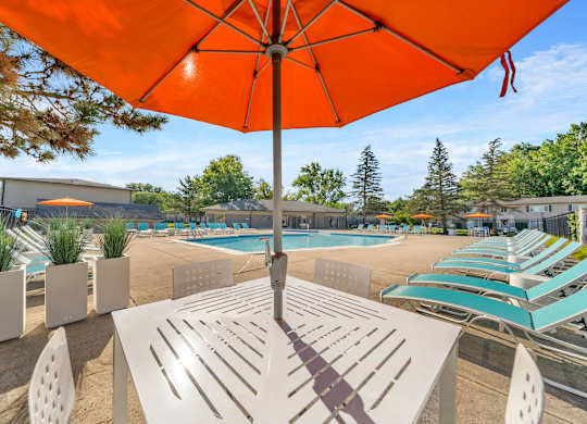 A sunny day at the poolside with a bright orange umbrella providing shade.