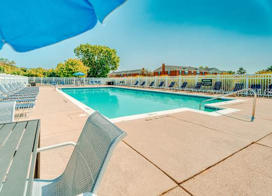 A pool with chairs and a table is surrounded by a blue umbrella.