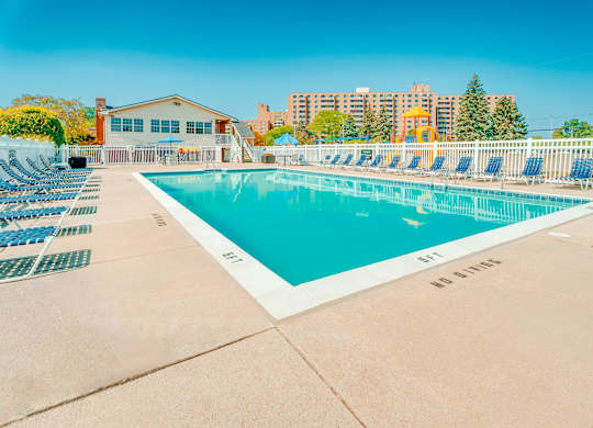 A large outdoor swimming pool surrounded by a white fence and lounge chairs.