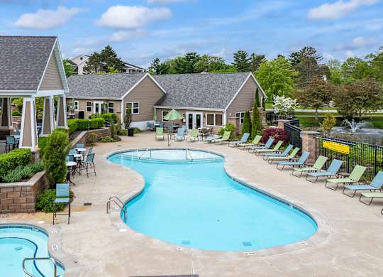 A large outdoor swimming pool surrounded by lounge chairs and a building in the background.