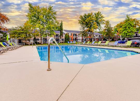 A swimming pool surrounded by trees and chairs.