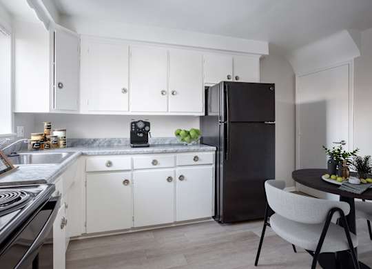 A black refrigerator stands in a kitchen with white cabinets and a marble countertop.