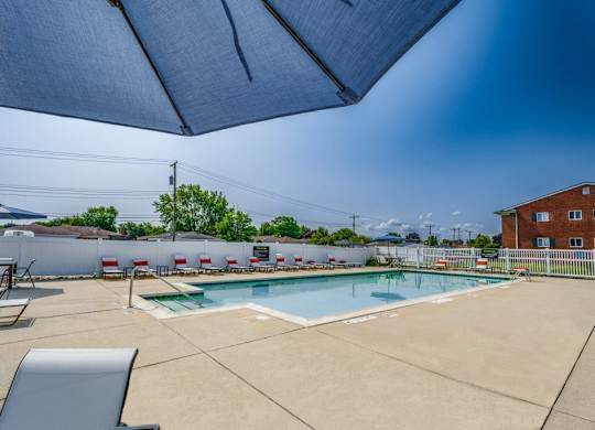 A pool area with a blue umbrella and a white fence.
