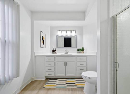 A white bathroom with a toilet, sink, and a rug on the floor.