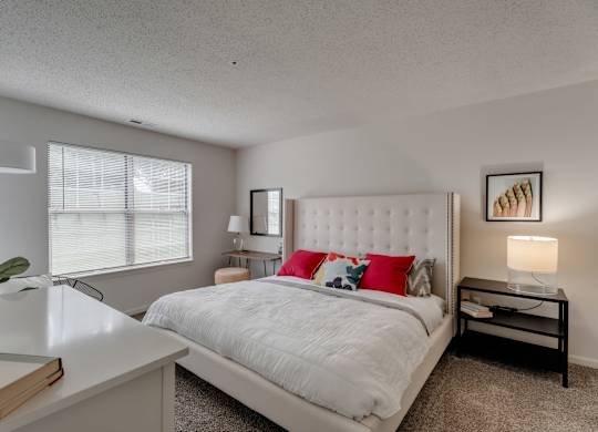 A bedroom with a white bed and a white nightstand with a lamp.