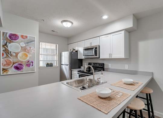 A modern kitchen with a stainless steel refrigerator, microwave, and a sink with a mat on the counter.
