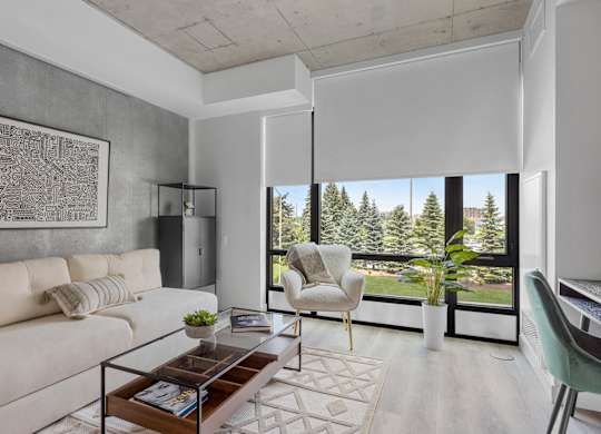 A living room with a white couch, a coffee table, and a large window with a view of trees.