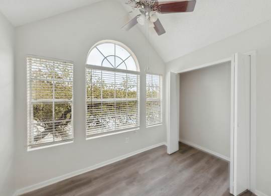 A room with a ceiling fan and a large window with blinds.