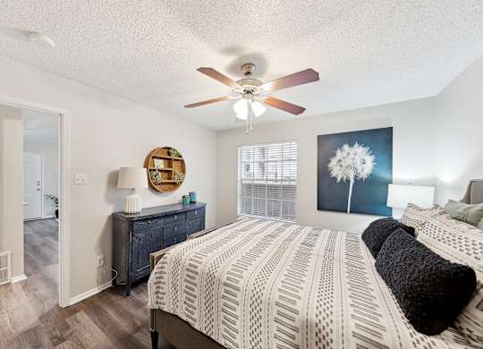 A bedroom with a bed, a ceiling fan, and a dresser.