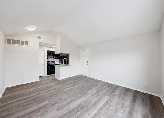 A room with a wooden floor and a kitchen area in the background.