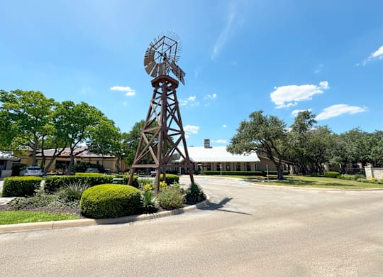 A windmill stands in the middle of a road with trees and bushes around it.