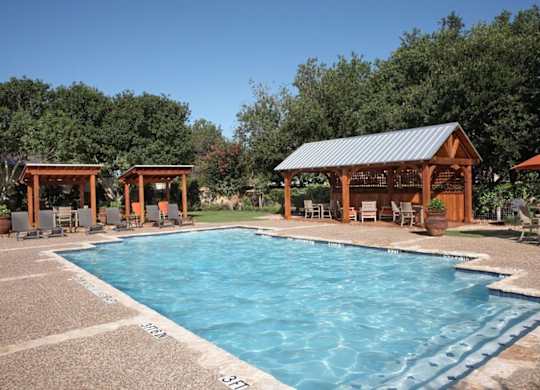 A large outdoor swimming pool surrounded by trees and wooden pavilions.