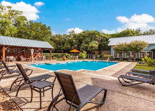 A pool area with lounge chairs and a pavilion.
