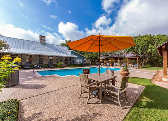 A patio with a table and chairs and an orange umbrella.