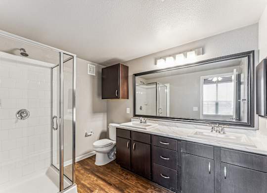 A bathroom with a white tiled shower, a white toilet, a sink with a mirror and a cabinet.