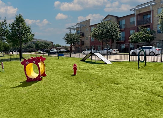 A playground with a red chicken slide and a red fire hydrant in a grassy area.