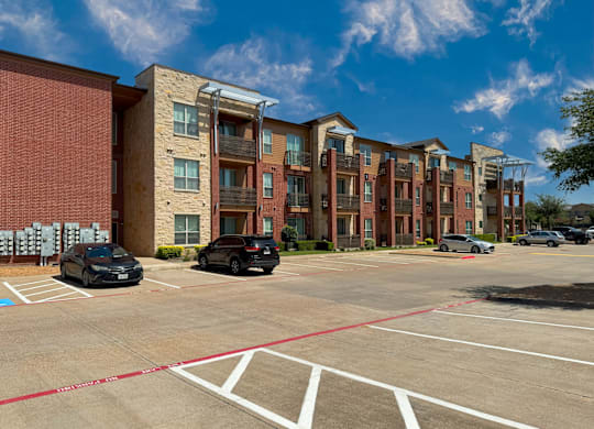 A parking lot in front of a multi-story apartment building with cars parked.