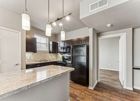 A kitchen with a black refrigerator and a marble countertop.