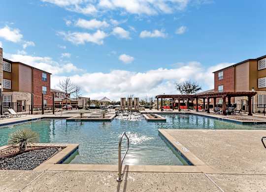 A pool area with a fountain in the middle and buildings in the background.