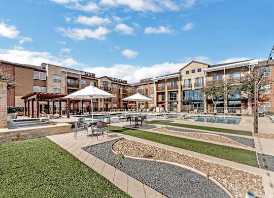 A sunny day at a courtyard with a grassy area, a fountain, and a building in the background.
