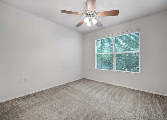A room with a ceiling fan and a window with a view of trees.