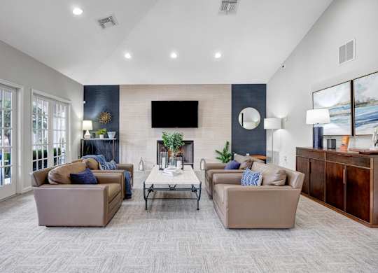 A living room with a grey carpet and a flat screen TV mounted on the wall.
