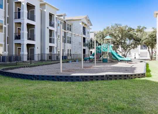 A playground with a green slide is surrounded by apartment buildings.