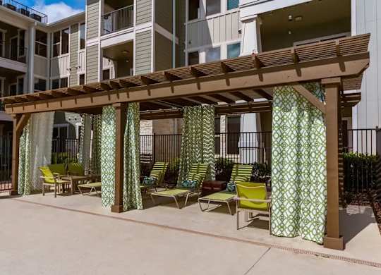 A patio with a wooden pergola and green chairs.