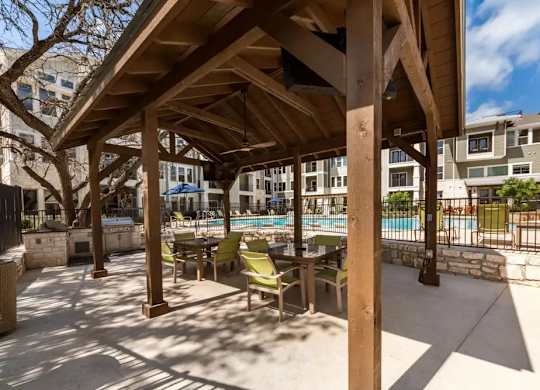 A wooden pergola over a pool with green chairs underneath.
