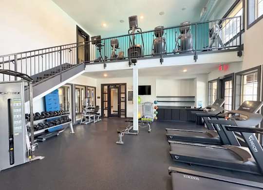 A gym with treadmills, weights, and a balcony.