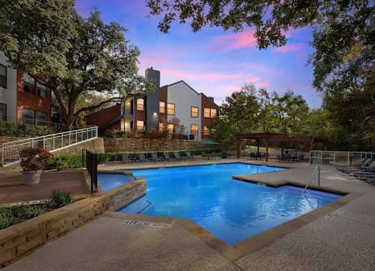 A swimming pool surrounded by a stone wall with a building in the background.