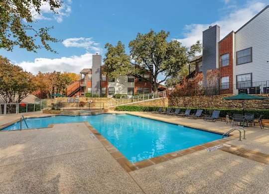 A swimming pool surrounded by a concrete deck and lounge chairs.