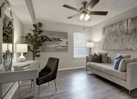 A living room with a grey couch, a chair, a table with a vase and a lamp on it, and a painting on the wall.
