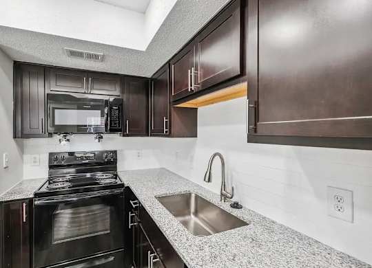 A modern kitchen with dark brown cabinets and a stainless steel stove top.