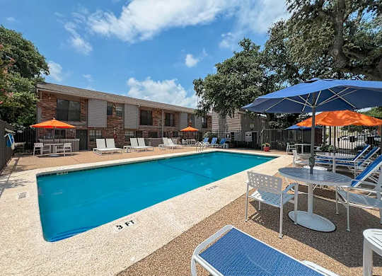 A pool with a blue umbrella and chairs around it.
