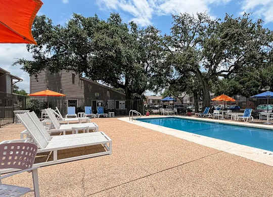 A pool surrounded by chairs and trees.
