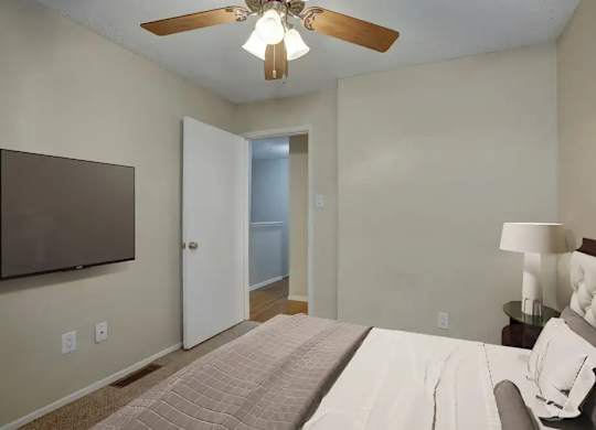 A bedroom with a bed, a ceiling fan, and a lamp.