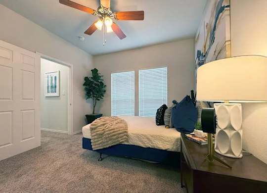 A bedroom with a bed, a ceiling fan, and a lamp.