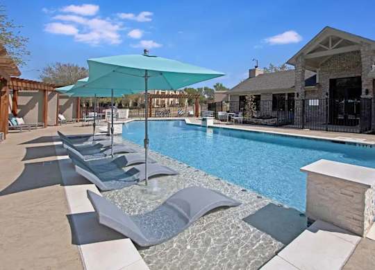A pool with a blue umbrella and lounge chairs.
